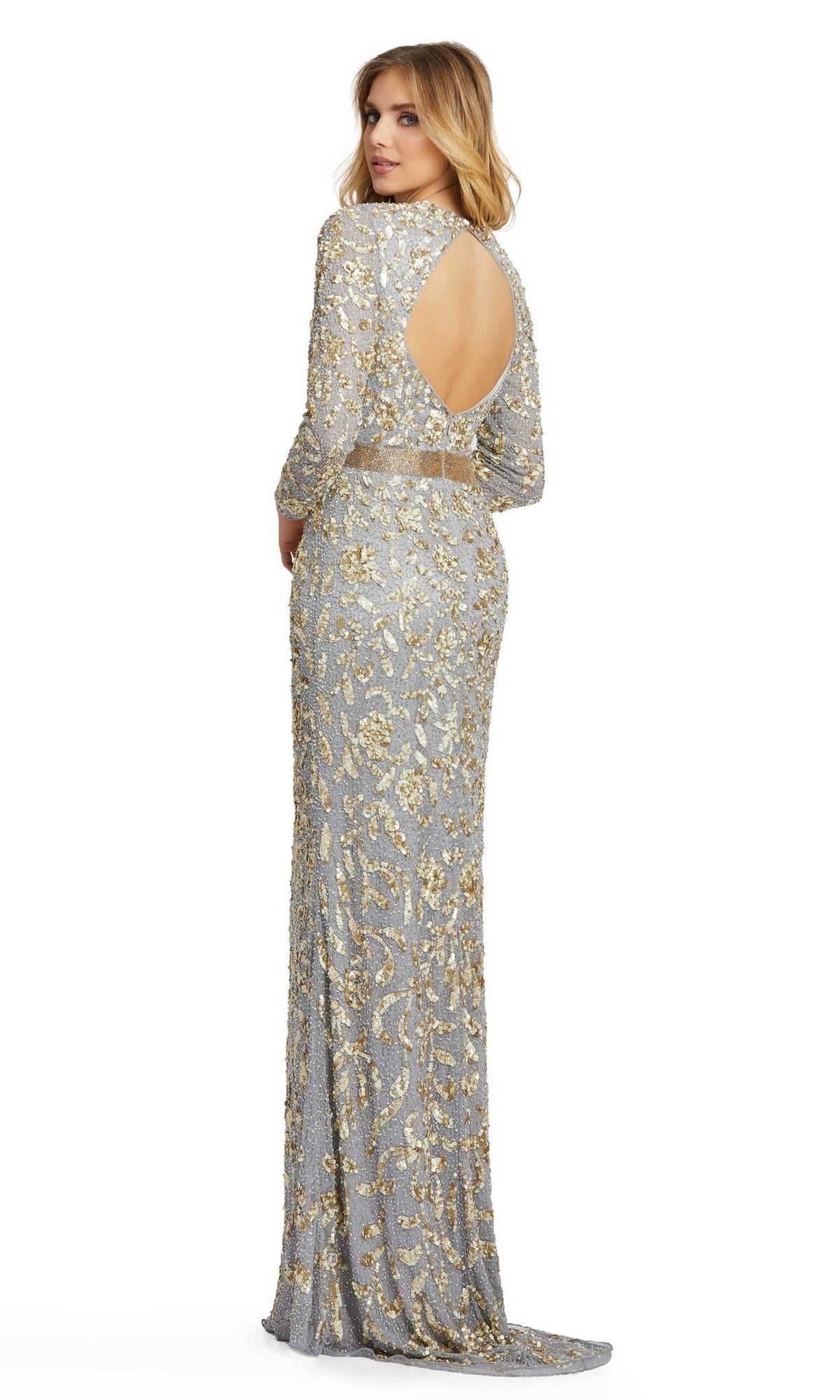 A woman stands looking over her shoulder, wearing the Long Formal Dress 4316 by Mac Duggal—an elegant floor-length platinum gown with gold sequin embellishments and a circular open back.